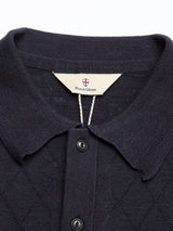 Close-up of the BGwally Diamond Polo in dark navy by Blue de Gênes, featuring a collar, black buttons, diamond knit pattern, and a label reading Blue de Gênes beneath a red and white shield logo.