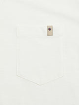 Close-up of Blue de Gênes BGoscar T-Shirt - Snow Fall’s white crewneck and pocket, with a beige tag above featuring a shield emblem with a red cross and blue border. Made from 100% cotton.