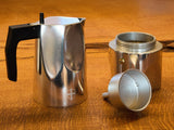 A disassembled Blue de Gênes BDG Coffee Maker - Grey with a black handle rests on a wooden surface, displaying its main pot, filter funnel, and base.