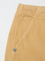 Close-up of a tan corduroy pocket on Blue de Gênes BGfloyd Cord Shorts in Pale Khaki, showing diagonal stitching and a small shield-shaped metal badge near the pocket.
