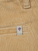 Close-up of BGfloyd Cord Shorts - Pale Khaki by Blue de Gênes, showing beige corduroy fabric, a pocket, and a stitched label with a shield featuring a red cross on white.
