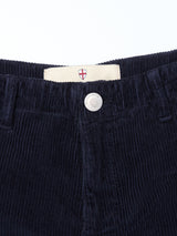 Close-up of the waistband of BGfloyd Cord Shorts - Dark Navy by Blue de Gênes, showing a silver button with embossed crest and a white fabric label bearing a red cross emblem above the button.