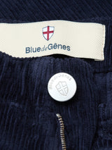 Close-up of BGfloyd Cord Shorts in Dark Navy by Blue de Gênes, showing a red cross shield logo label and a metal button engraved with the brand name and logo above a partially open zipper.