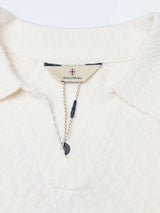 Close-up of the BGjohn Slubby Polo in Chalk by Blue de Gênes—a cream textured knit shirt with John collar, V-neck opening, branded fabric tag, and navy string with button detail for a classic vintage leisurewear look.