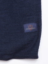 Close-up of Monte Knit - Navy, a cotton/linen blend fabric. A small rectangular patch displays a logo with an orange shield outline and the text Blue de Gênes in orange on a dark blue background.