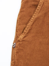 The Paulo Tucan Chino - Biscotto by Blue de Gênes features a close-up of brown comfort stretch corduroy showcasing a pocket with decorative stitching and a small patch with a white cross. The ribbed texture typical of corduroy is highlighted, made in Italy against a pristine white background.