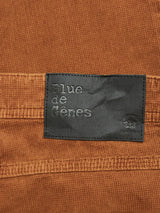 Close-up of the Paulo Tucan Chino - Biscotto by Blue de Gênes, showcasing brown comfort stretch corduroy fabric with a black leather patch. The patch has embossed text Blue de Gênes, an emblem with a bridge, and Il ponte di Rialto, enhancing its charm. These regular fit jeans are made in Italy.
