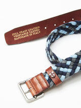 The Pratese Belt - Blue by Blue de Gênes features braided cotton webbing in blue, grey, and black with a leather strap and silver buckle. Accompanying it is a brown full-grain leather belt embossed with Vegetable Tanned, Handmade in Italy.