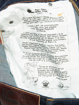 Close-up of Repi Dai V Dark Jeans by Blue de Gênes, featuring a white label about architecture and denims significance. The comfort stretch material enhances ease and style, while a leather patch and metal buttons highlight the regular slim-fits detailed design in dark blue denim.