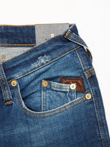 A close-up of a Repi Dragon Dark Used Jeans pocket in denim blue by Blue de Gênes shows visible stitching and brass rivets. A leather patch is above the pocket, with a tag in the waistband. These regular slim-fit jeans offer comfort stretch denim for easy movement.