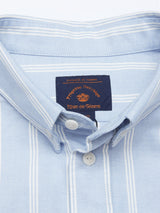 Close-up of the Sandro Caicos Shirt - Blue Stripe, crafted from 6oz fine stripe fabric, featuring white vertical stripes on light blue. The label displays Blue de Gênes in red and black. Made in Somelos, Portugal, it has a neatly folded collar with two white buttons.