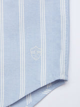 The Sandro Caicos Shirt by Blue de Gênes is a light blue Oxford piece with vertical white stripes, made from 6oz fine stripe fabric. It features an embroidered shield emblem at the bottom right, highlighting the exquisite craftsmanship of Somelos in Portugal.