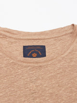 Close-up of a Totti T-Shirt - Tuape by Blue de Gênes, highlighting its beige linen texture. The round neckline reveals a blue label with orange text and logo stitched inside the collar.