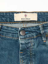 Close-up of Blue de Gênes Vinci Topaz Vintage Jeans - Used, highlighting the blue denim waistband, black shield-embossed button, orange stitching, and a white Blue de Gênes label with red and white shield logo.