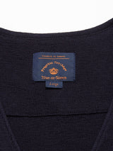 Close-up of the Zorba Knit Waistcoat - Navy from Blue de GĂȘnes, with a label reading VeraestĂ di Genova, Progetto Heritage, and size Large. Accented with corozo nut buttons, it is displayed on an off-white surface.