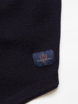 Close-up of a navy woven fabric made from Merino wool with a small blue rectangular patch featuring a red-orange Blue de GĂȘnes logo and suede&coos, similar to details on the Zorba Knit Waistcoat.