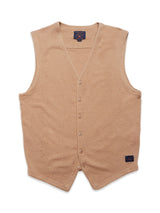 The Zorba Knit Waistcoat - Taupe by Blue de Gênes is showcased against a white backdrop. This beige, V-neck, sleeveless knit waistcoat with corozo nut buttons is made from merino wool and features a small label near the bottom edge.