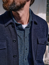 A bearded man models the Blue de Gênes Enrico Cord Shirt - Blue Pattern over a collared shirt and white undershirt. The shirt features black buttons and two chest pockets. His face is partially out of frame, showing only his neck and part of his jawline.