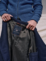A person in a blue sweater holds open a navy Peacoat - Dark Navy, showcasing the Melton wool lining and Blue de Gênes label, featuring classic peacoat details and branded buffalo horn buttons.