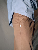 A person wears a light blue shirt with Blue de Gênes Menzo Dobby Chino - Brownie, featuring a small logo on the pocket. Captured from the side, the photo showcases the comfort stretch of these chinos, blending style with flexibility in every move.
