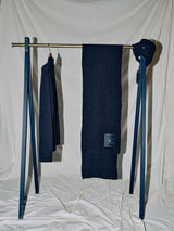 A clothing rack showcases the Oscar Croft Beanie in Dark Navy by Blue de Gênes, paired with a dark sweater and a long 5-gauge knit scarf, all set against a neutral beige draped background.