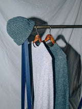 The Oscar Melange Beanie - Forest by Blue de Gênes, made from a cozy wool blend, looks great with a blue scarf, light and dark gray sweaters. All items are stylishly displayed on a clothing rack against a chic beige fabric backdrop.