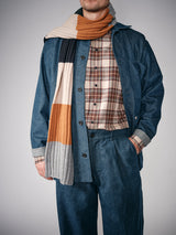 A person wearing a blue denim jacket and pants, a Blue de Gênes Robertino Brush Shirt in Stone, and a multicolored ribbed scarf in gray, cream, orange, and navy; only the lower part of their face is visible.