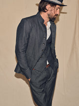 A man in a stylish gray suit and high-collared jacket stands sideways against a plain background, his outfit elevated by an Italian handmade gray fedora with a decorative band. The vintage sophistication of the ensemble is enhanced by Blue de Gênes Pento Belt in rich brown full-grain bull leather.