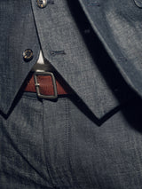In a close-up, a person wears a dark gray suit with a vest and trousers. The Pento Belt - Brown by Blue de Gênes, handmade in Italy from full grain bull leather with a rectangular metal buckle, adds elegance at their waist.