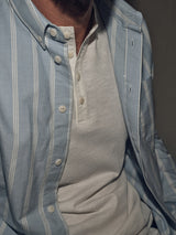 A person is wearing the Sandro Caicos Shirt - Blue Stripe by Blue de Gênes, made from 6oz fine stripe fabric from Somelos, Portugal. Its styled casually over a white shirt, partially open to highlight its quality.