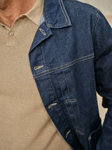 A person wears the Blue de Gênes Cosimo Trucker Jacket in Dark Blue Denim over a beige, textured knit shirt, focusing on the jackets stitching and the shirts pattern across the upper torso.