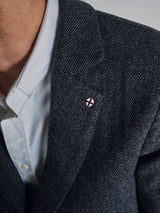 A person wearing the Fukui Blazer – Black Pattern by Blue de Gênes and a white dress shirt, accessorized with a lapel pin featuring a red cross on white, perfectly exemplifies the appeal of relaxed tailoring.