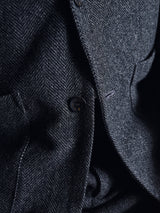 Close-up of the Fukui Blazer - Black Pattern by Blue de Gênes, showcasing relaxed tailoring details—a button, lapel, and pocket—with the texture and herringbone weave of this workwear jacket clearly visible.