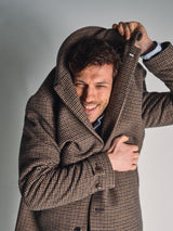 A man smiles playfully while pulling the collar of his Blue de Gênes Massone Check Coat - Multi Check over his head, partially covering his face. He stands against a plain, light background.