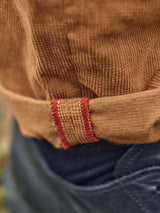 Close-up of someone sporting a Blue de Gênes Paulo Tucan Chino in Biscotto, featuring red stitched sleeves and fine Italian craftsmanship. Textured fabric is highlighted by rolled cuffs, paired with regular-fit jeans for an effortlessly stylish appearance.