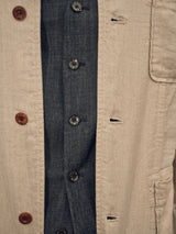 A close-up of the Gabbiano Winnot Blazer - Natural by Blue de Gênes, showcasing its beige herringbone-patterned cotton-linen fabric with brown buttons, layered over a dark denim shirt featuring black buttons with intricate white designs to emphasize the fastening details and textures.