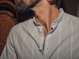 Close-up of a man’s neck and lower face, highlighting his beard. He wears a partially open collar on his light blue Basso Hackney Shirt - Blue Stripe by Blue de Gênes, subtly showcasing its refined craftsmanship.
