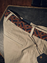 Beige pants lie on a textured surface, featuring the Pratese Belt - Brown by Blue de Gênes. This handcrafted belt showcases brown, blue, and gray hues with vegetable tanned leather accents and a tag at the loop, reflecting elegance and quality craftsmanship made in Italy.