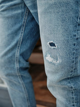 Close-up of Vinci Super Used Jeans by Blue de Gênes, showcasing a distressed patch on the knee with a visible tear and frayed edges. These regular fit jeans, expertly crafted in Italy, combine style and durability effortlessly.