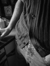 A black-and-white close-up features a person in jeans and the Blue de Gênes Compra Open Polo Knit in Dark Navy. Theyre leaning against a counter with one hand partially visible, exuding a casual, retro vibe enhanced by organic cotton fabric and retro stitch detailing.