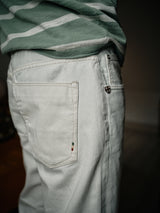 Someone is wearing the Giacomo Bull WTH - White Denim by Blue de Gênes, featuring stone-washed white denim with a small Italian flag near the back pocket. A green and white striped shirt complements this Italian-made ensemble, highlighting the back pocket and side zipper.