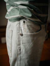 A person sports a green and white striped shirt with the Giacomo Bull WTH - White Denim by Blue de Gênes. These Italian-made stone-washed jeans feature a small emblem near the pocket, with visible fabric texture and stitching, offering a casually comfortable style.