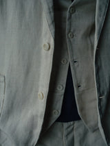 Close-up of a person wearing the Pantella Desk Gilet - Natural by Blue de Gênes, paired with a light-colored suit featuring Corozo buttons and a left-side pocket. Crafted from a Cotton/Linen blend, the textures stand out against a softly blurred background.