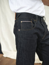 Close-up of a person wearing Giacomo Selvedge Jeans - Raw Denim by Blue de Gênes with a white shirt. The jeans highlight Italian craftsmanship with visible stitching and metal rivets against a softly blurred indoor backdrop.