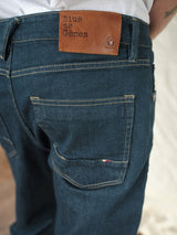 The person is facing away from the camera, wearing Blue de Gênes Vinci Topaz Jeans in rinse wash, featuring a brown leather label on the waistband. Made in Italy, these jeans show visible stitching and back pockets, providing style and comfort with stretch denim.