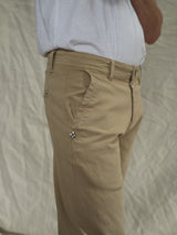 Wearing Blue de Gênes Menzo Dobby Chino in khaki, featuring a side emblem and comfort stretch, the individual pairs them with a white shirt. Theyre viewed waist-down against a light, textured background, emphasizing the vintage style of their outfit.