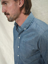 A man with a mustache stands sideways against a light background, wearing a Sandro Chambray Shirt by Blue de Gênes.