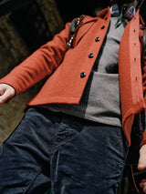 Low-angle shot of a person wearing a red coat over the Monte AW Knit - Stormy Grey by Blue de Gênes and dark pants, standing in an urban setting. Their head isnt visible, and they have a backpack strap over one shoulder.