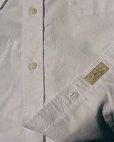 A close-up of the BGsander Oxford Shirt - White by Blue de Gênes, crafted from 100% cotton, featuring cream buttons and a small beige label with text on the pocket. The shirt’s fine stitching and smooth fabric texture are clearly visible.