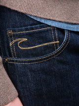 Close-up of the front pocket of Blue de Gênes Marco Rinse Jeans in rinse wash, crafted from 100% cotton dark blue denim with yellow stitching, partially covered by a brown sweater and a blue shirt.